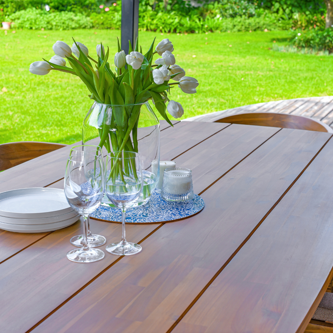 Wine glasses, white plates, candles and a vase placed on a wooden table - close up image facing the garden