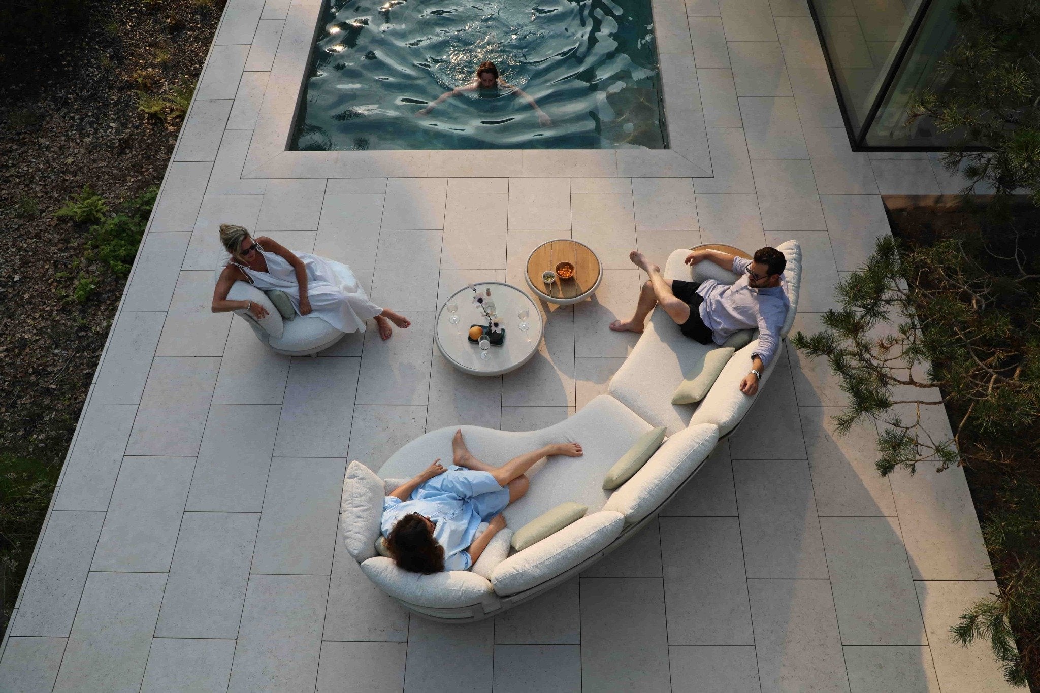 Modern curved lounge seating and coffee tables showcasing outdoor furniture in South Africa beside a contemporary pool patio.